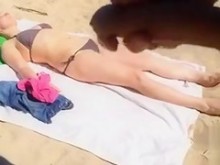 Masturbándose mientras una mujer en bikini yace en la playa
